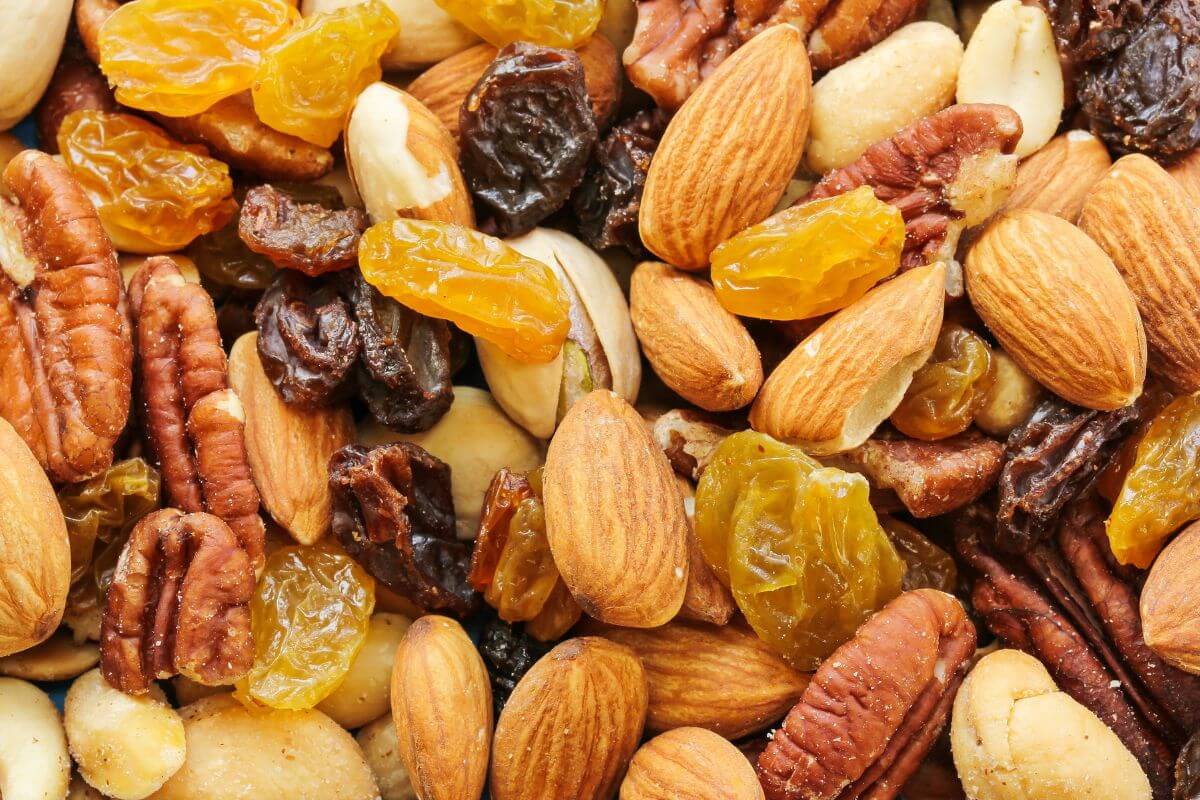 A variety of mixed nuts and dried fruits, including almonds, pecans, cashews, golden raisins, and dark raisins. 
