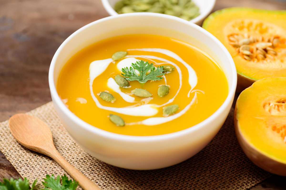 A bowl of creamy squash soup garnished with a swirl of cream and squash seeds.