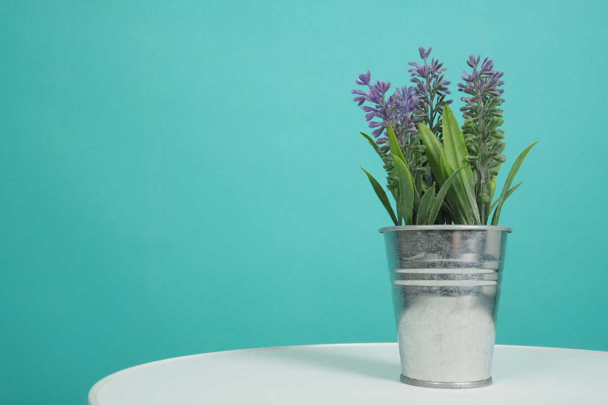 A silver metal pot filled with green leaves and purple lavender flowers sits on a white, round table. 