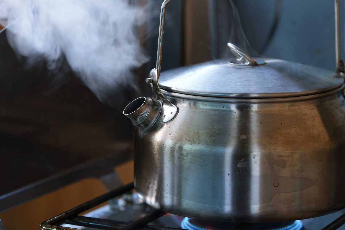 A stainless steel kettle steaming and whistling on a gas stove burner, indicating boiling water inside.