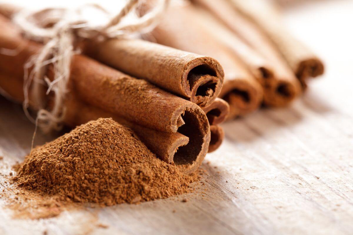 Close-up of several whole cinnamon sticks bound together with rustic twine, lying on a wooden surface.