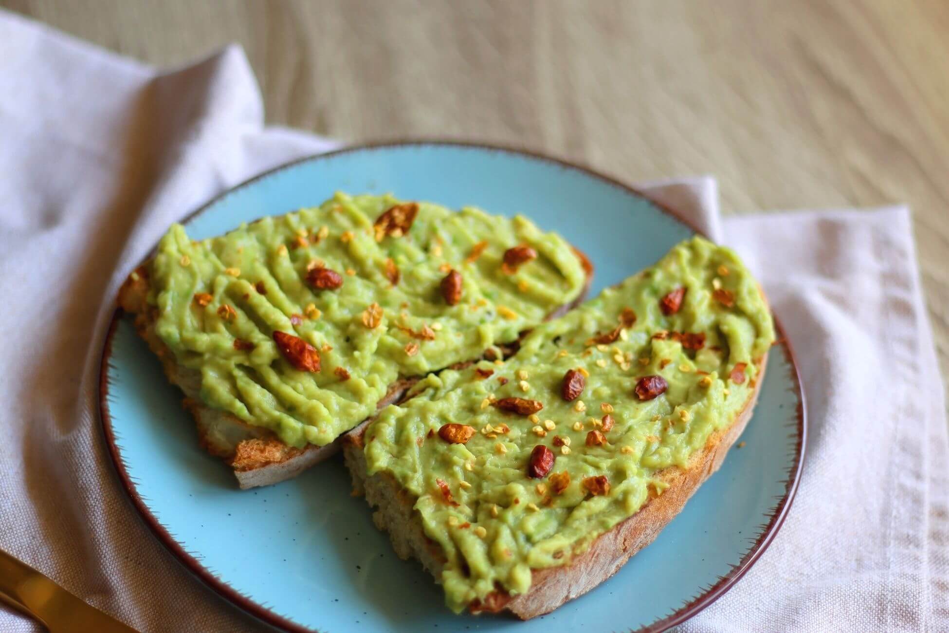 A light blue plate holds two slices of avocado bread topped with mashed avocado, garnished with red chili flakes. 