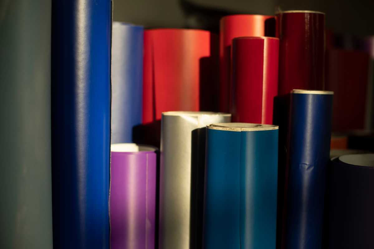 Multiple rolls of glossy papers in various colors, including blue, red, purple, and white, are standing upright. The scene is dimly lit with shadows.