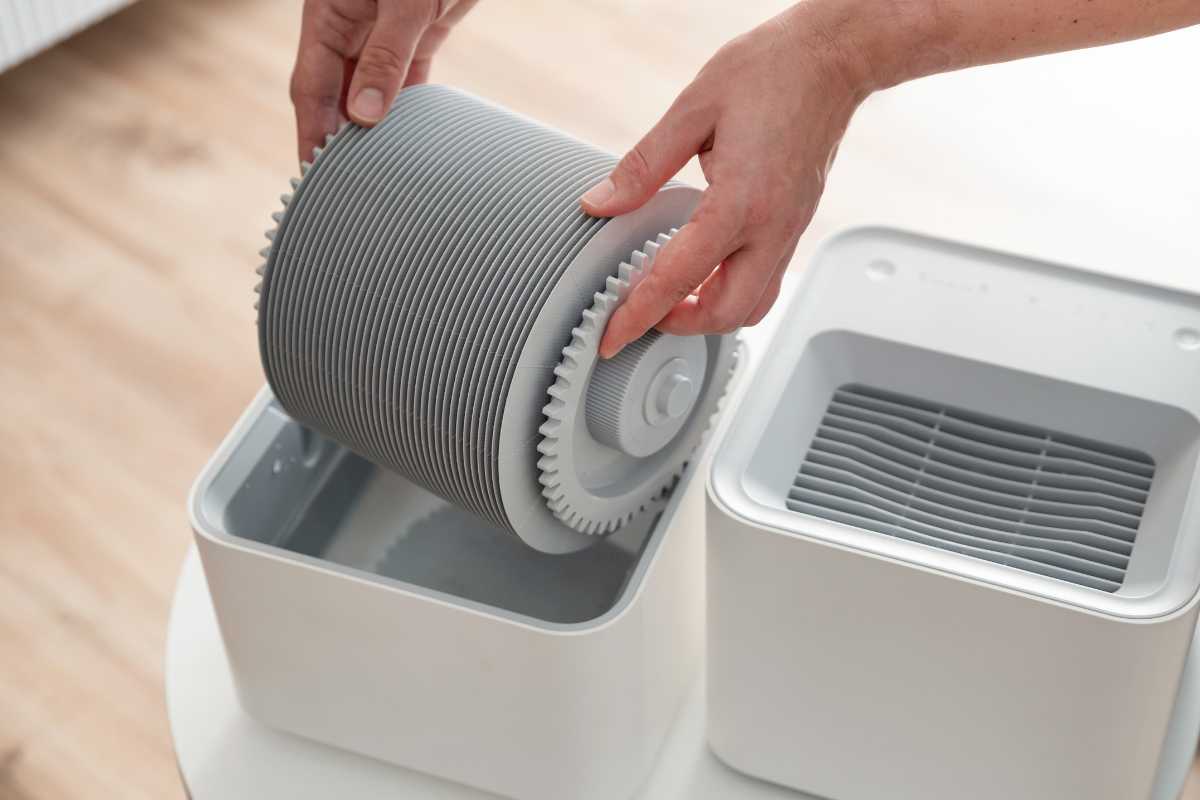 A person is placing a cylindrical filter into a compact, square-shaped humidifier. 