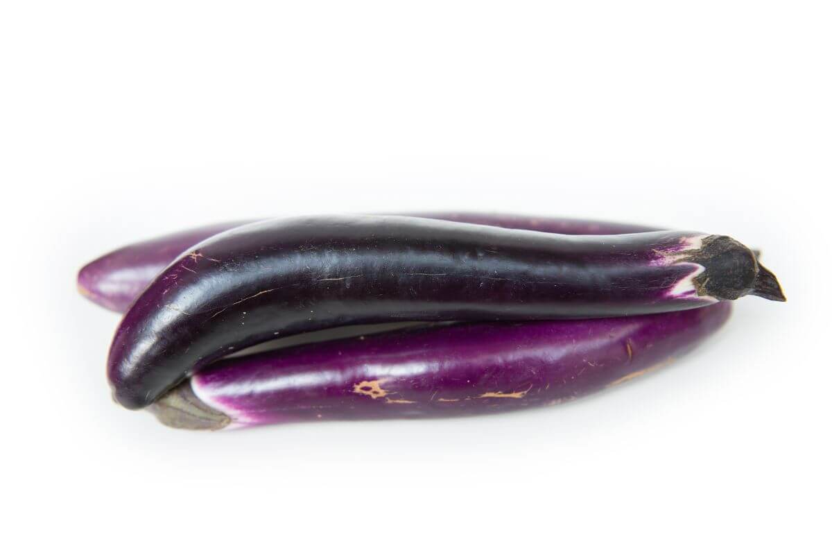 Three glossy purple Japanese eggplants, elongated and slightly curved, stacked on a white background.