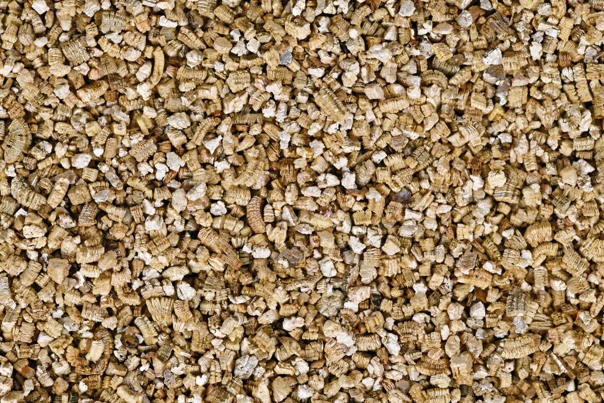 A large amount of small, crumbled, and irregularly shaped beige and light brown vermiculite granules. 