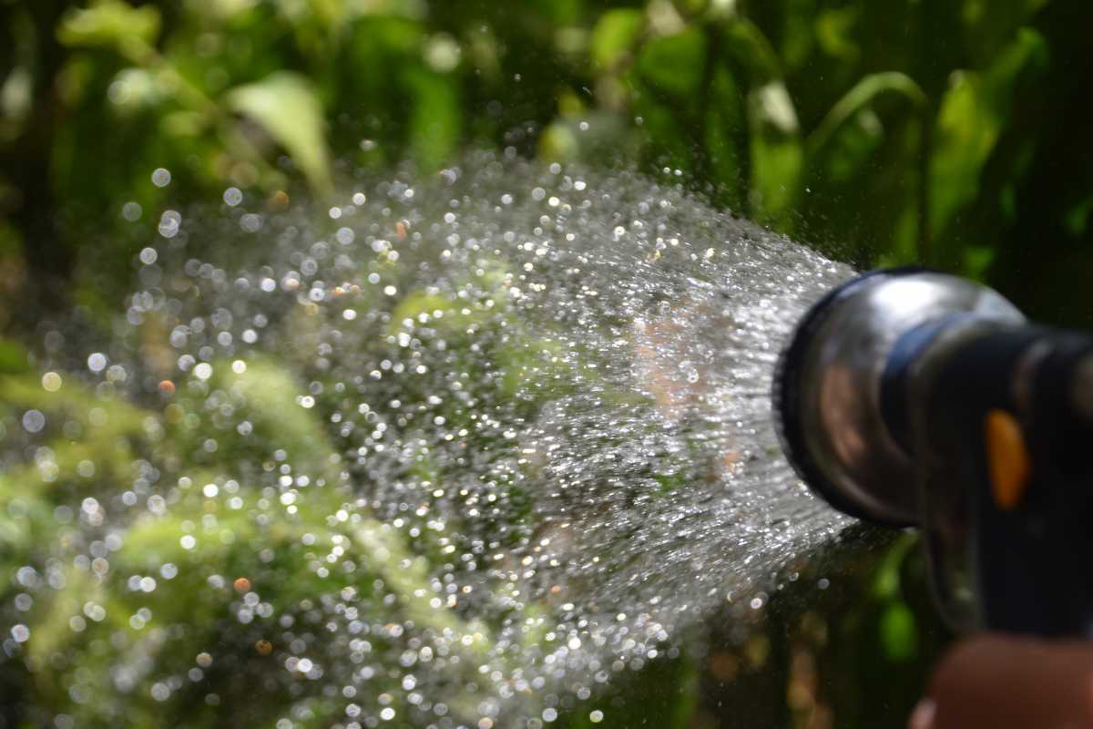 A garden hose nozzle spraying water. The water droplets are captured in mid-air, creating a misty effect.