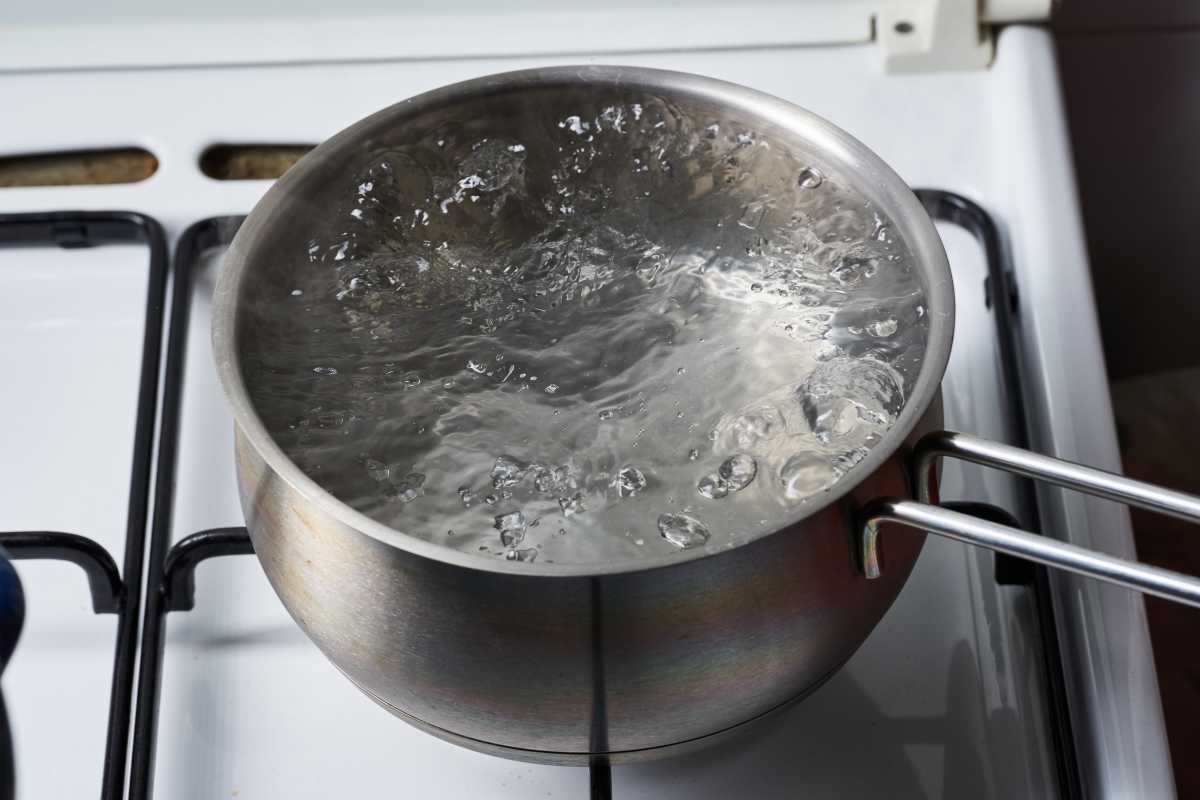 A stainless steel pot with water boiling vigorously on a gas stove. 