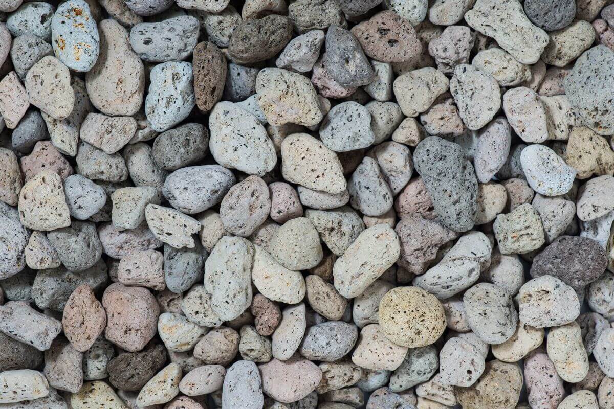 Close-up of a pile of variously sized and shaped pumice rocks with shades ranging from light grey to beige and some with speckled textures.