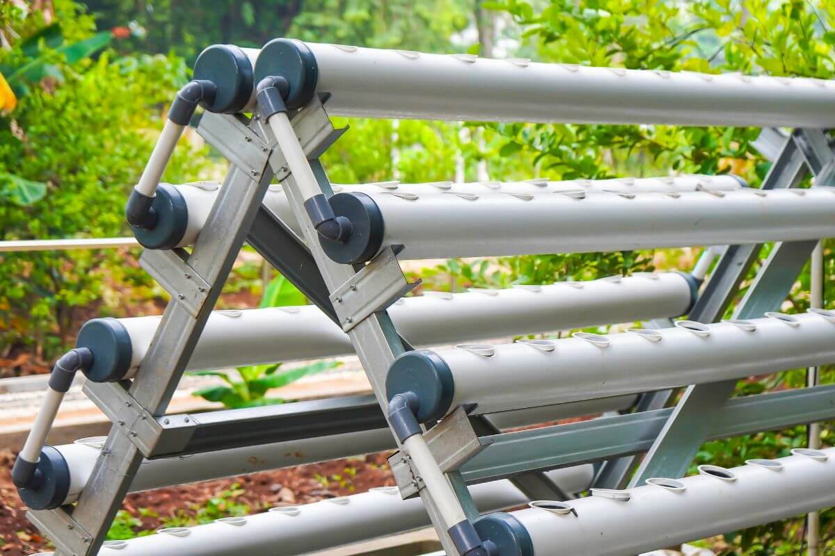 Close-up of an outdoor hydroponics system with multiple horizontal pipes arranged in a vertical A-frame structure.