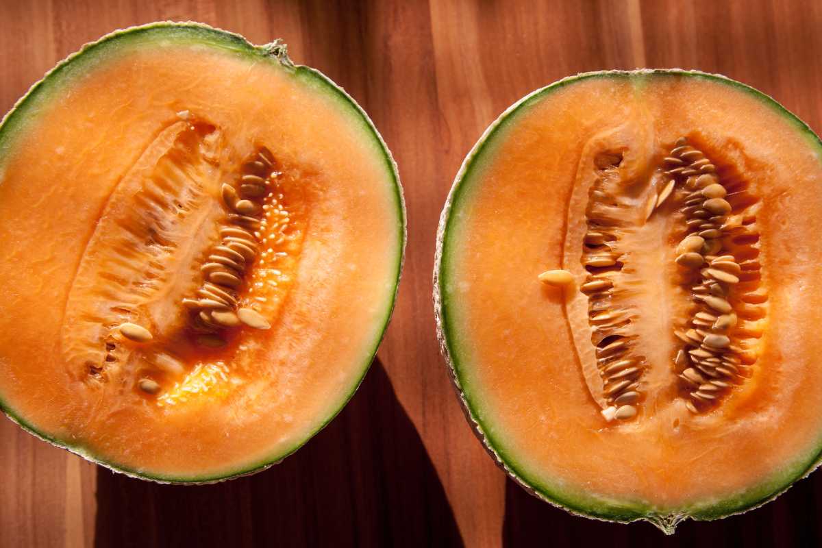 Two halves of muskmelon are displayed on a wooden surface, showcasing the bright orange flesh and seed-filled center. 