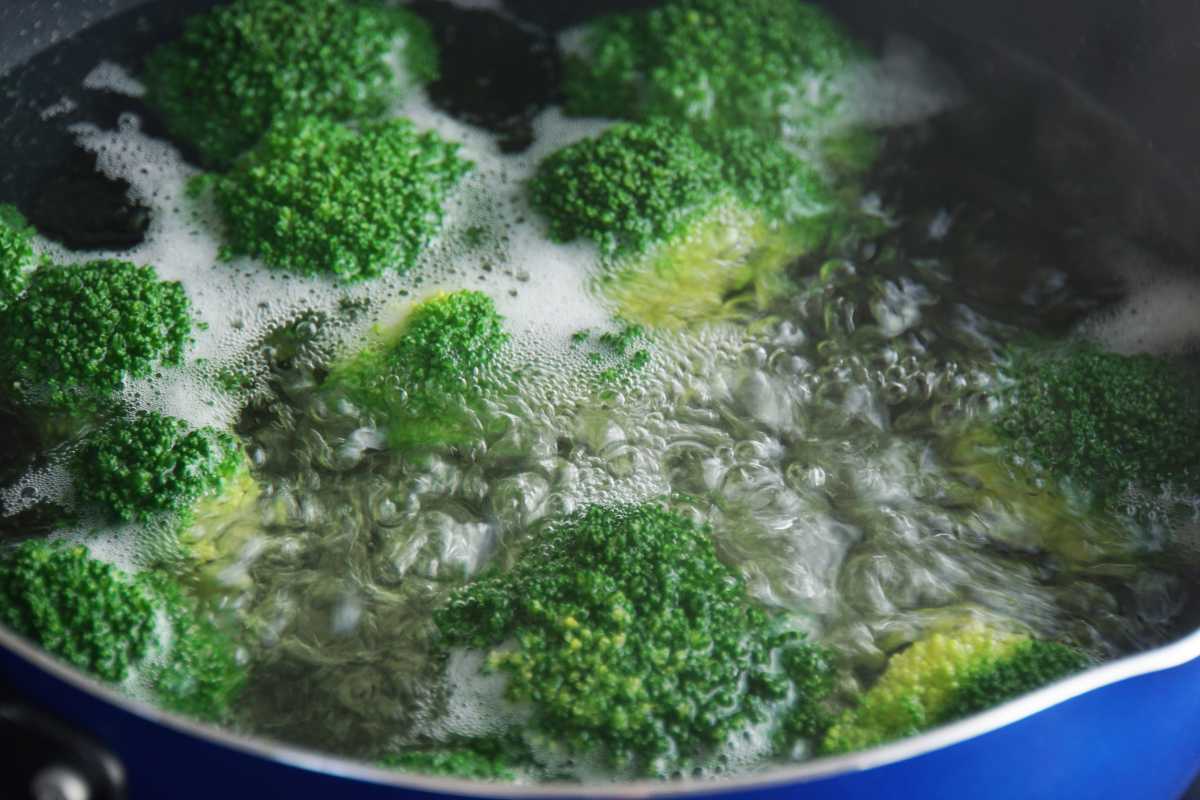 Broccoli florets boiling in water with bubbles and steam in a close-up view inside a blue pot. 