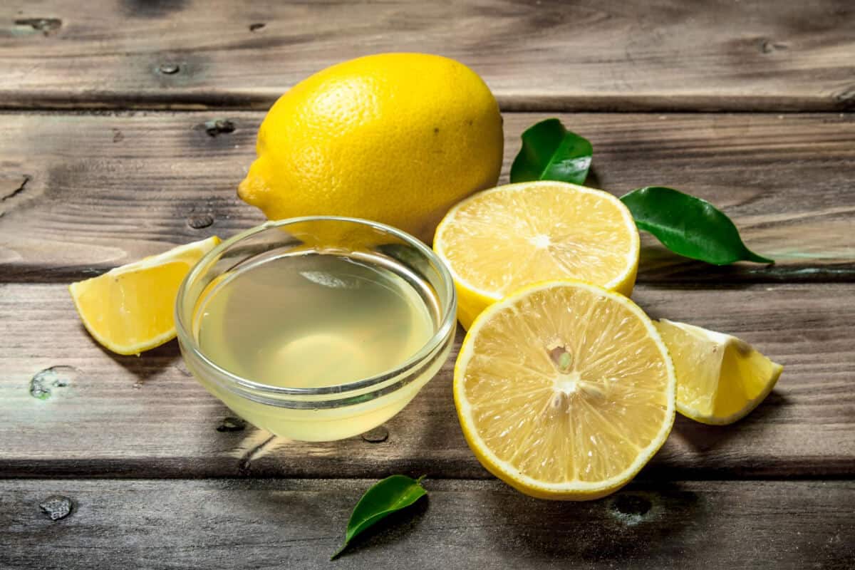 A whole lemon, lemon halves, and lemon wedges are arranged on a wooden surface.