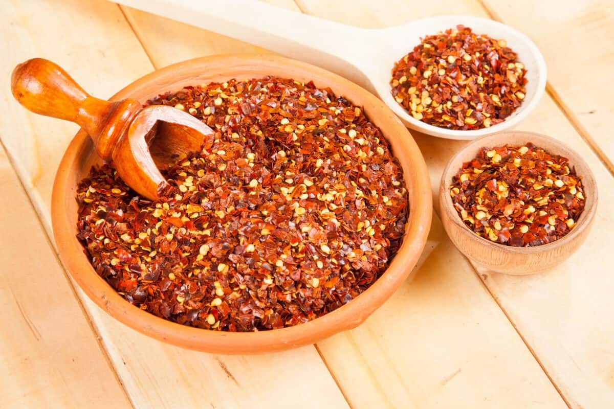 A ceramic bowl filled with cayenne pepper, a wooden scoop resting on top.